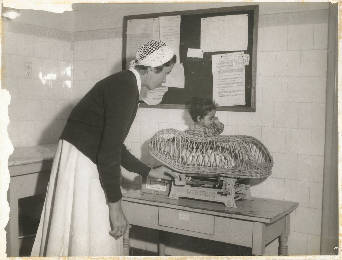 enfermeira pesa uma criança em um cesto sobre a balança
